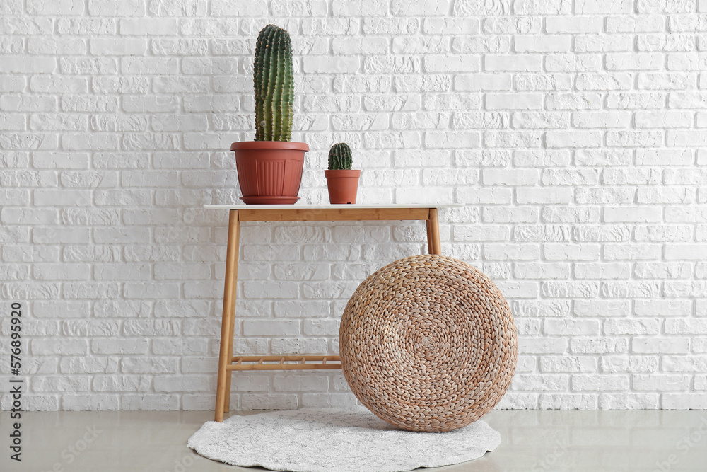 Table with green cacti and pouf near white brick wall