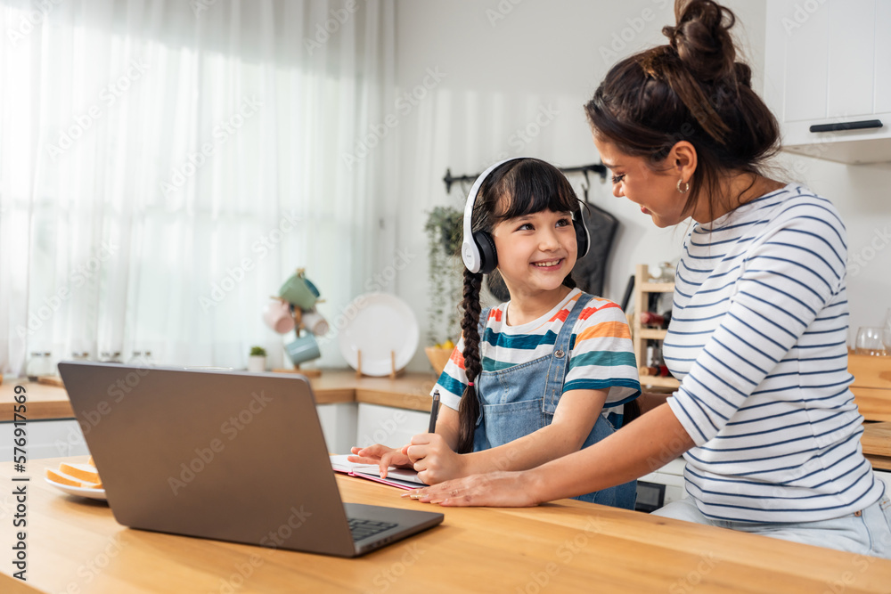 Caucasian young girl kid learning online class at home with mother.