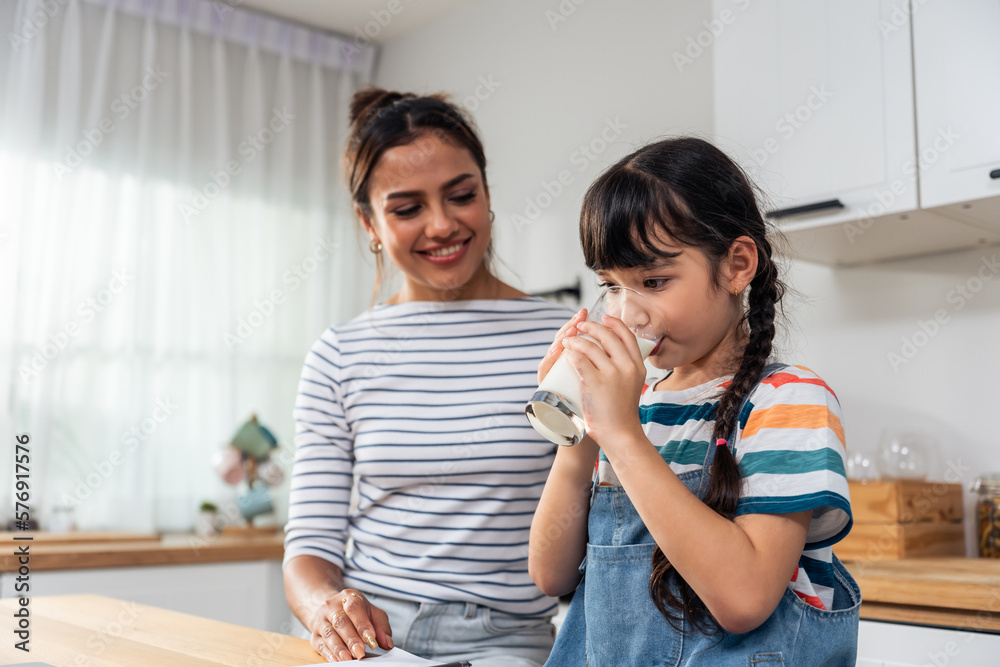 Caucasian little kid holding a cup of milk and drinking with mother. 