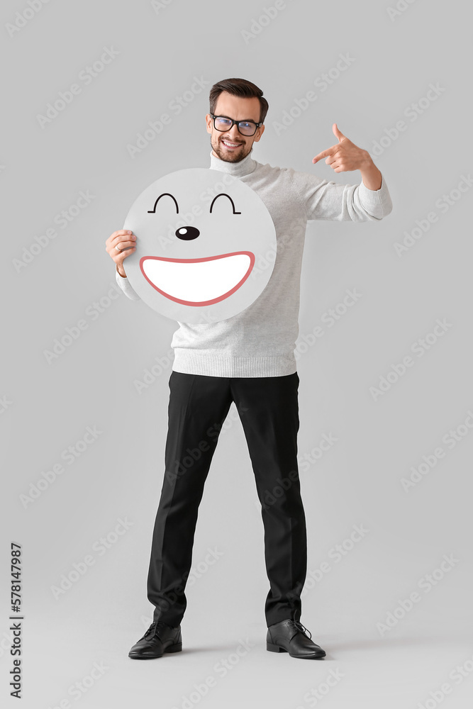 Happy man holding paper with smiling emoticon on light background