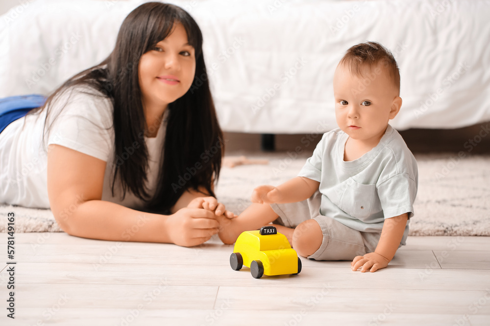 Baby boy playing with toy car and his mother in bedroom