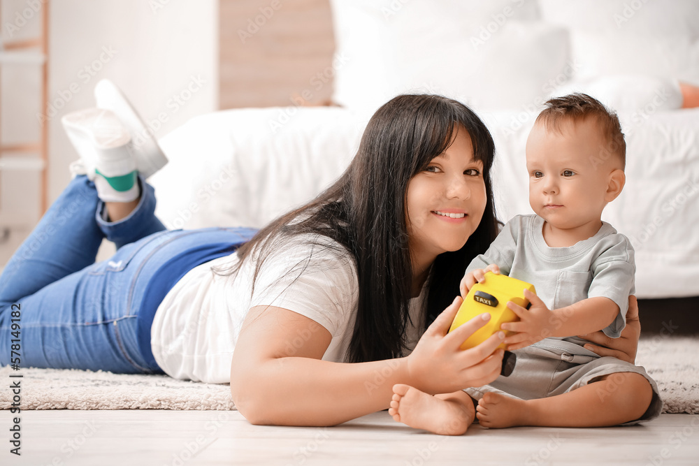 Baby boy playing with toy car and his mother in bedroom