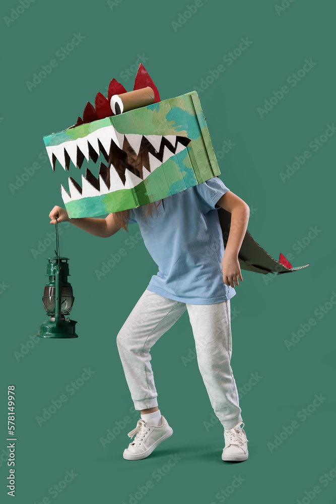 Little girl in cardboard dinosaur costume with lantern on green background