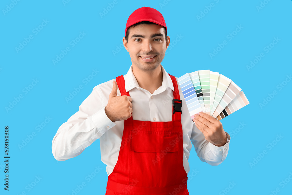 Male painter with color palettes showing thumb-up on blue background