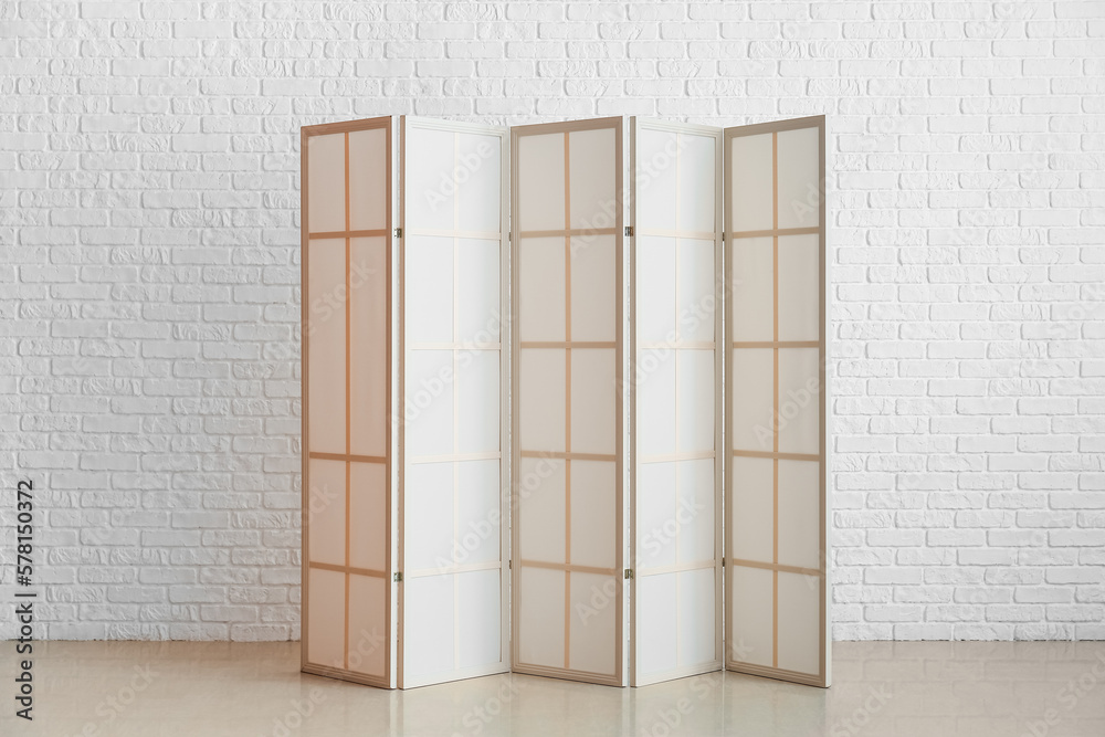 Beige folding screen near white brick wall