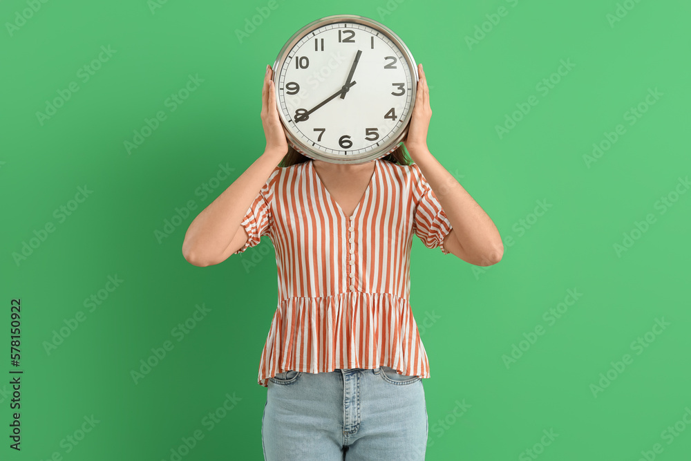 Young woman with wall clock on green background