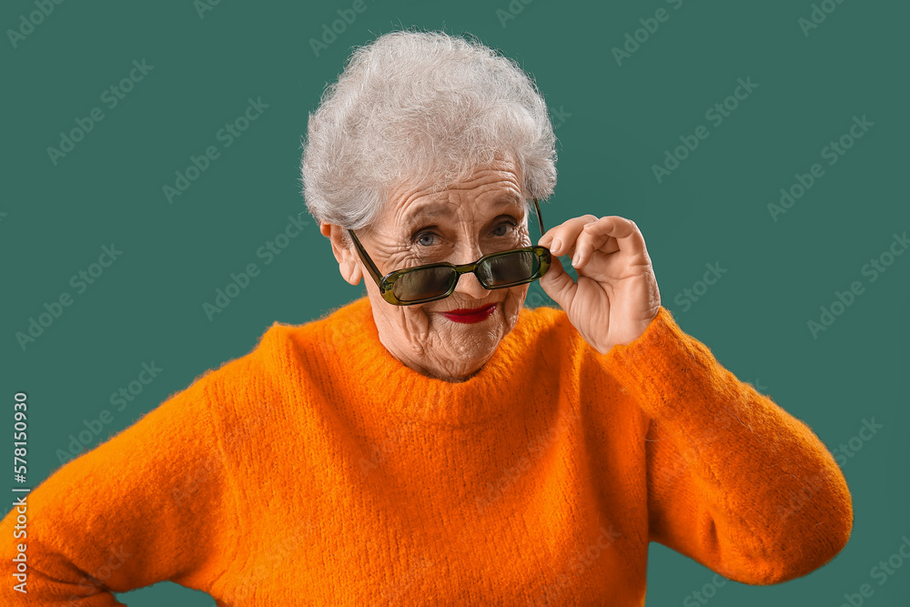 Senior woman in sunglasses and orange sweater on green background, closeup