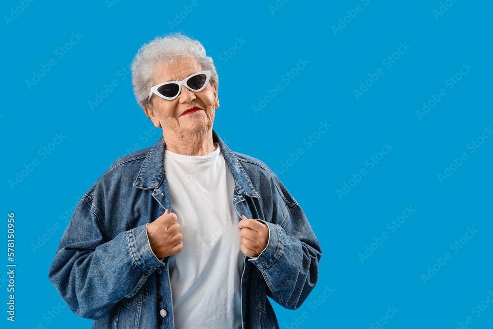 Senior woman in sunglasses and denim jacket on blue background