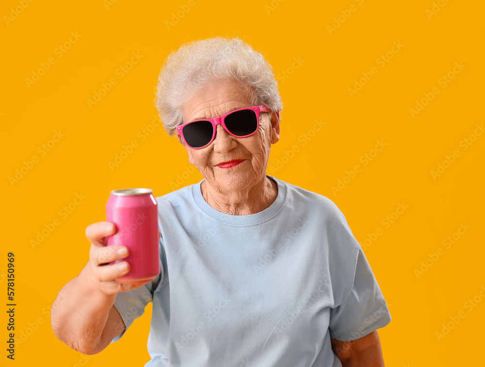 Senior woman in sunglasses with can of soda on yellow background