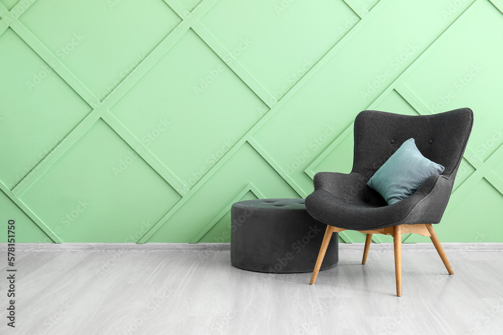 Stylish grey armchair, cushion and pouf near green wall