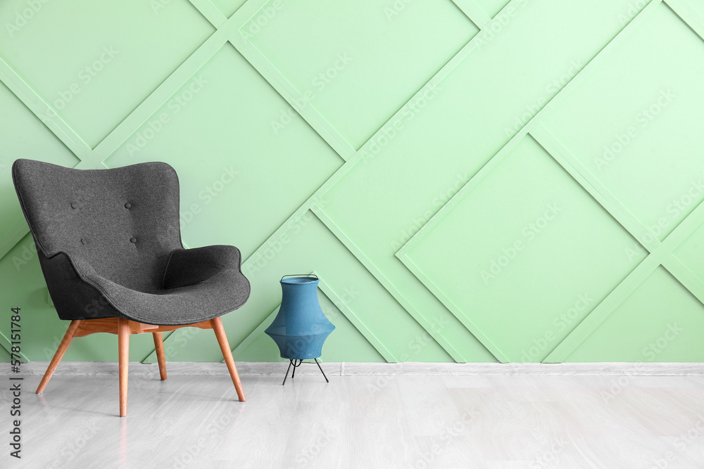 Stylish grey armchair and lantern near green wall