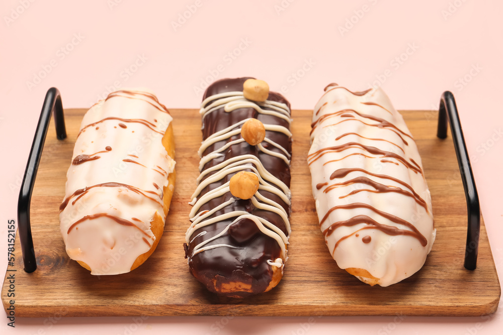 Board with delicious eclairs on pink background