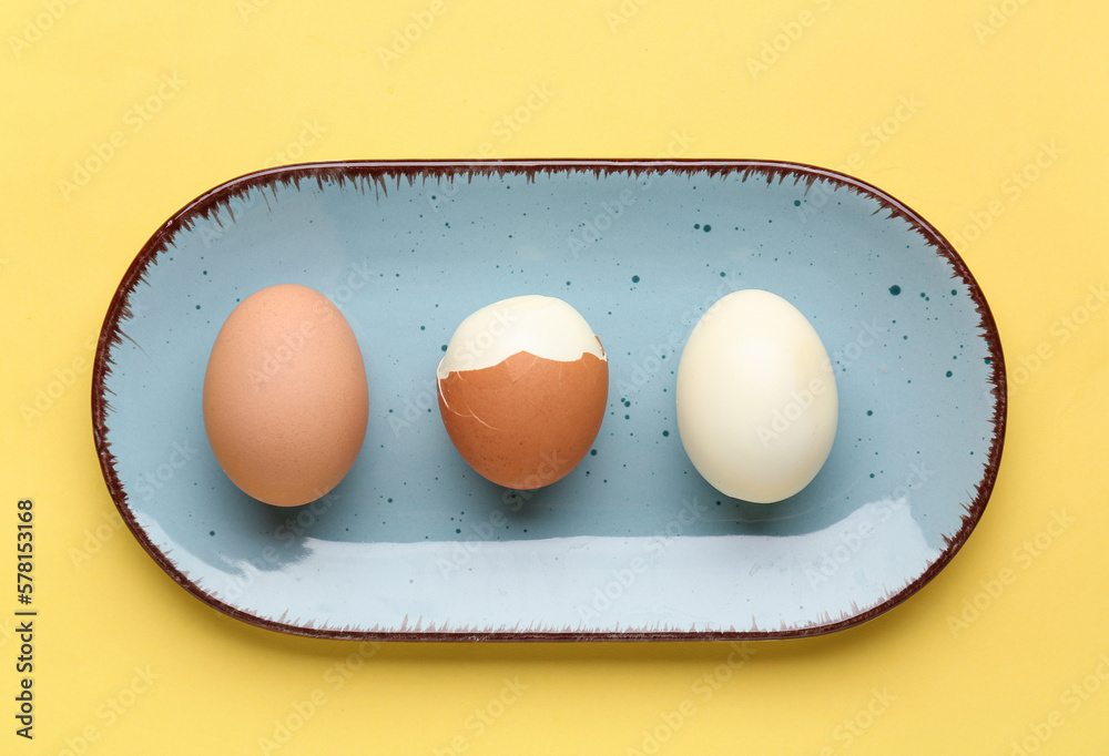 Plate with peeled and unpeeled boiled eggs on yellow background