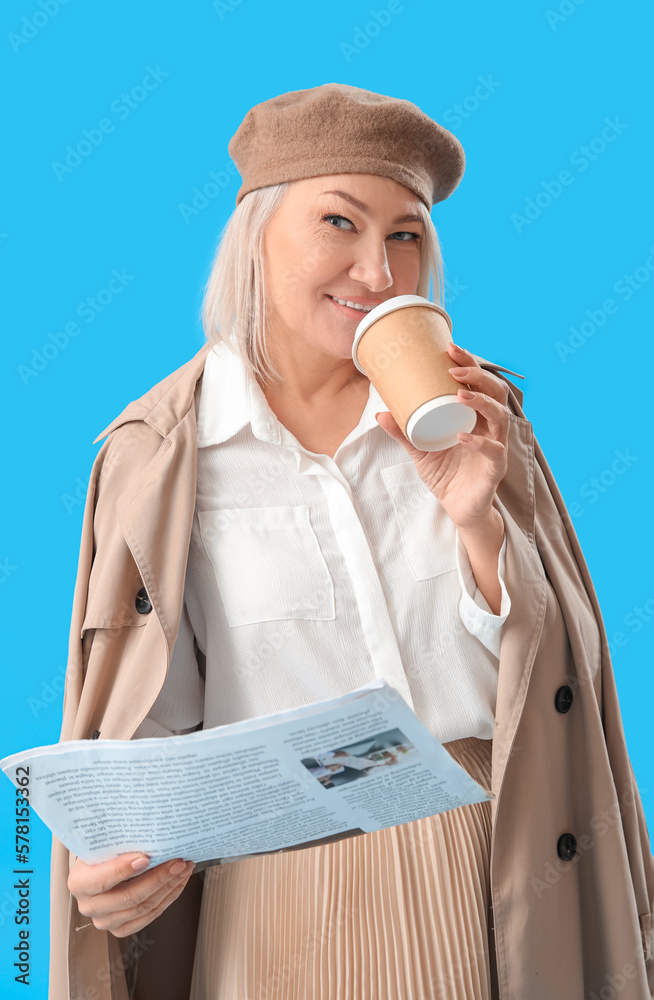 Stylish mature woman with coffee and newspaper on light blue background