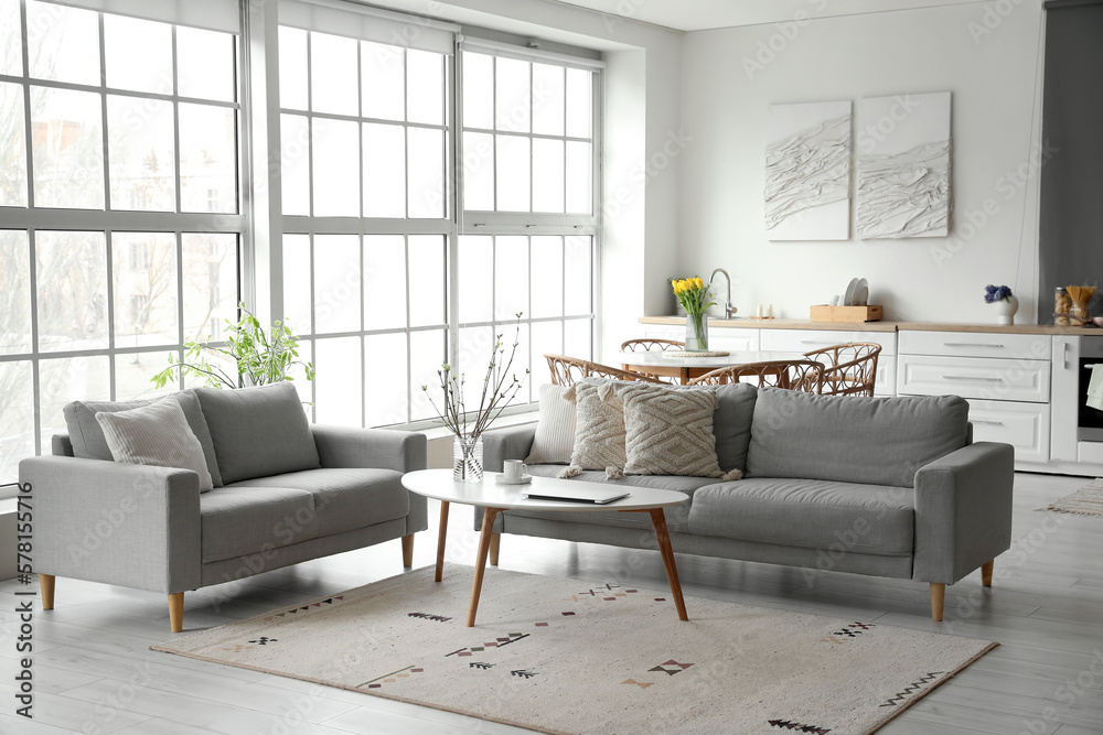 Interior of modern kitchen with grey sofas, dining table and counters