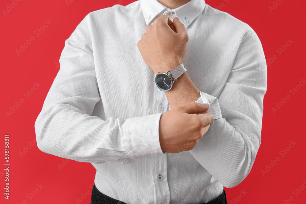 Young businessman rolling up his sleeve on red background, closeup