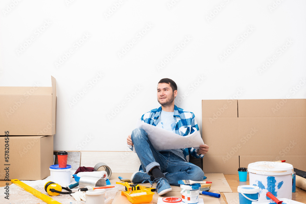 Happy guy sitting on floor with blueprint