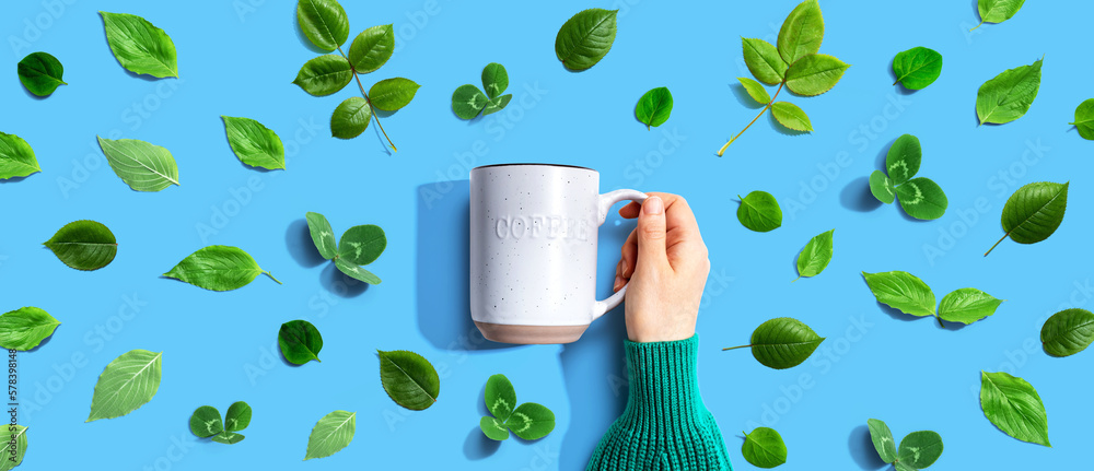 Person holding a mug with green leaves - flat lay