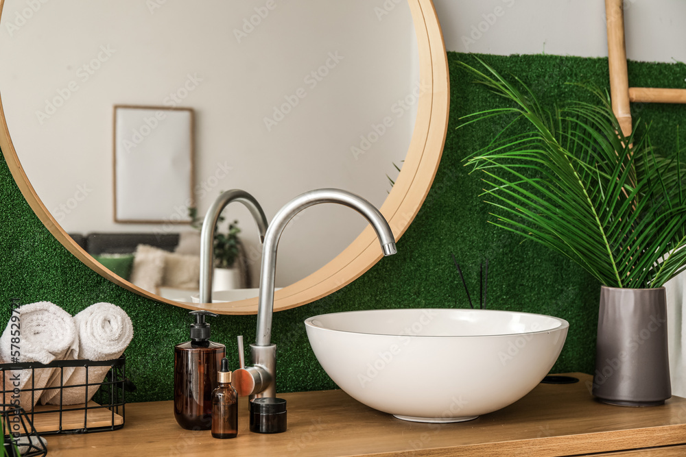 Vase with palm leaves, sink and cosmetic products on table in bathroom