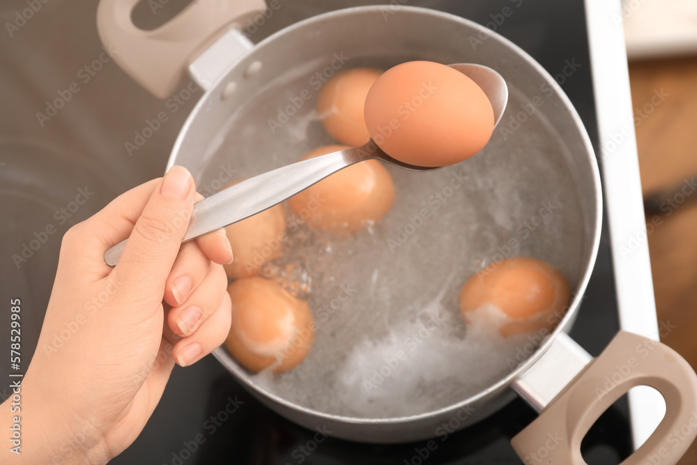 Woman holding spoon with boiled egg above cooking pot in kitchen, closeup