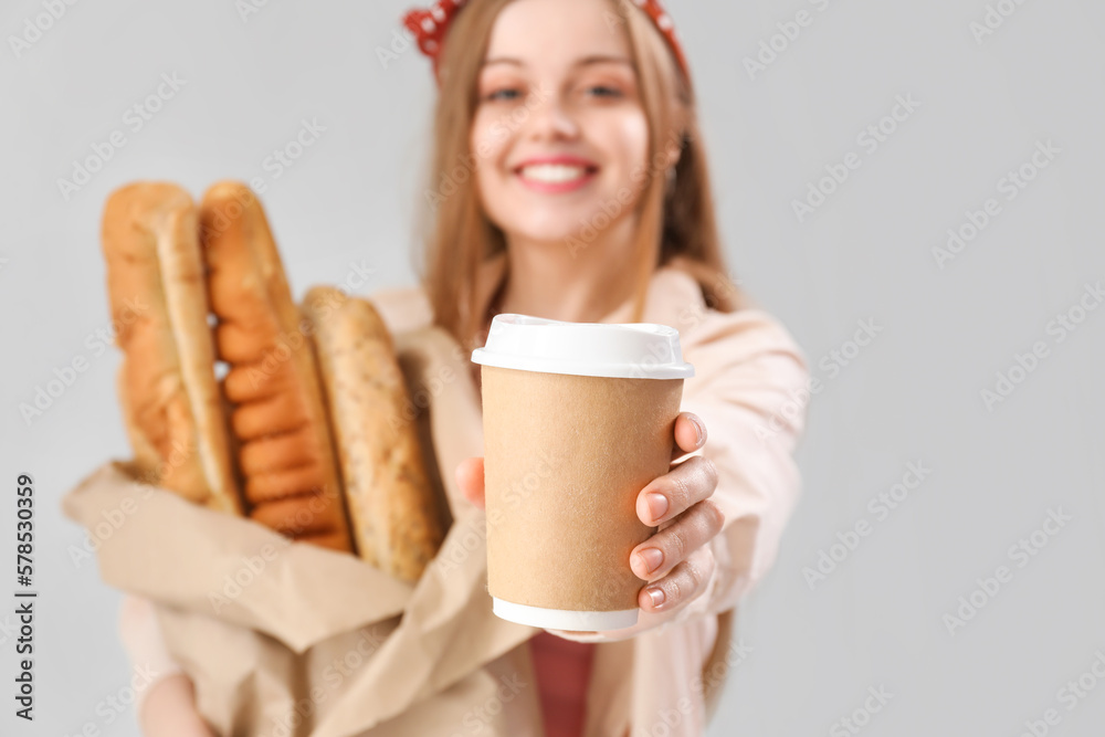 Young woman with fresh baguettes and cup of coffee on grey background, closeup