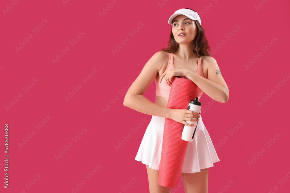 Sporty young woman with bottle of water and mat on pink background