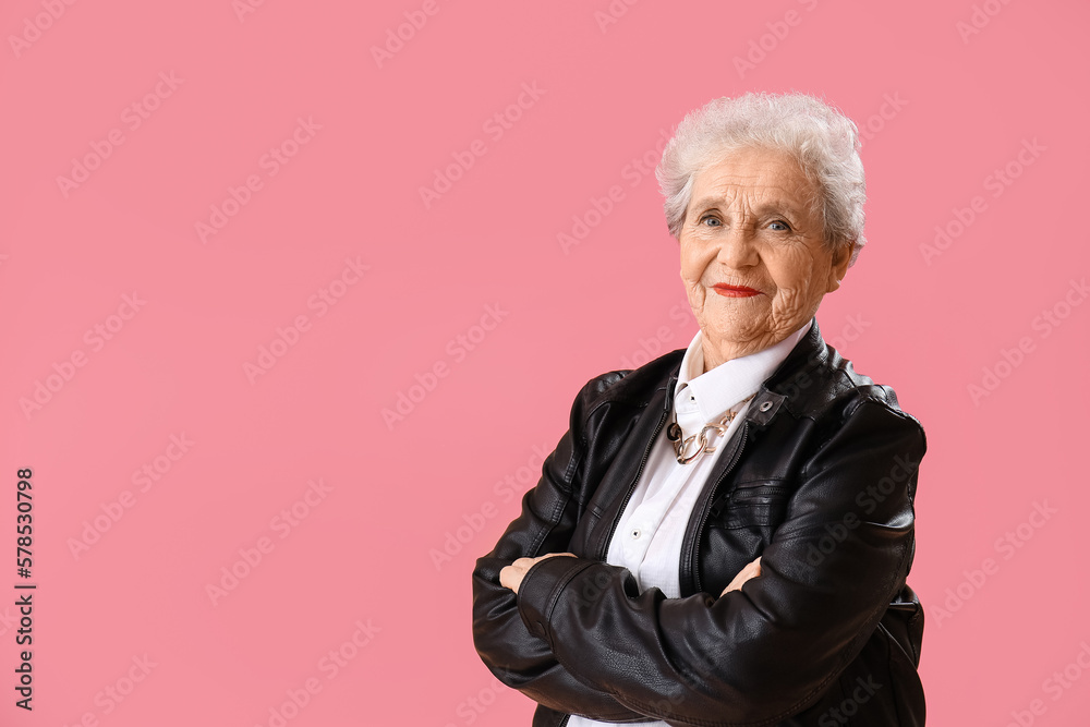 Senior woman in leather jacket on pink background