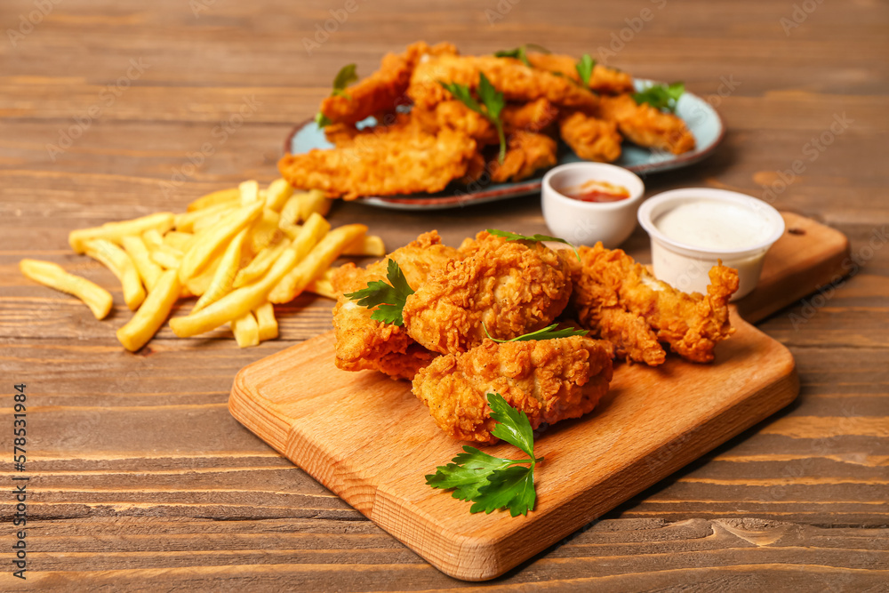 Board with tasty nuggets, sauces and french fries on wooden background