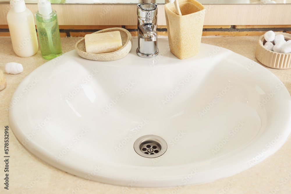 Table with white ceramic sink and bath supplies in room, closeup