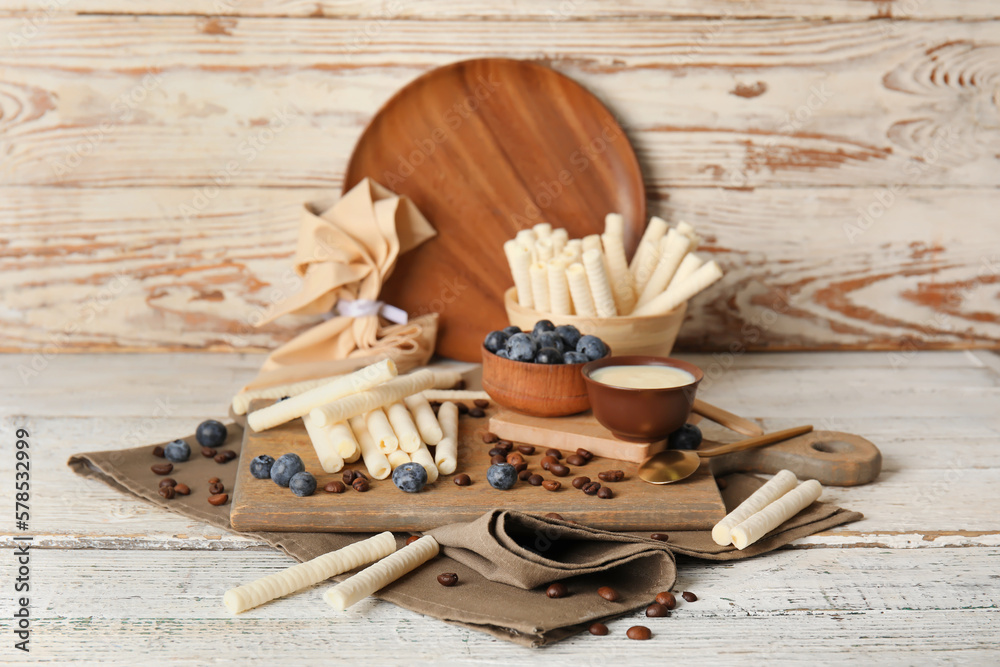 Board with delicious wafer rolls, blueberries and coffee beans on white wooden table