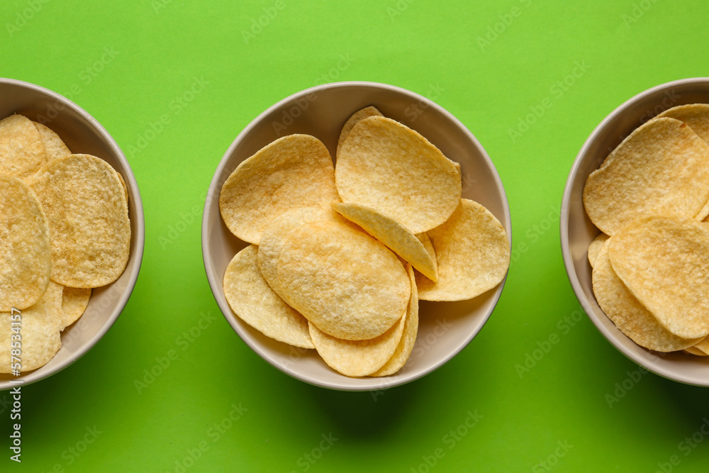 Bowls with delicious potato chips on green background