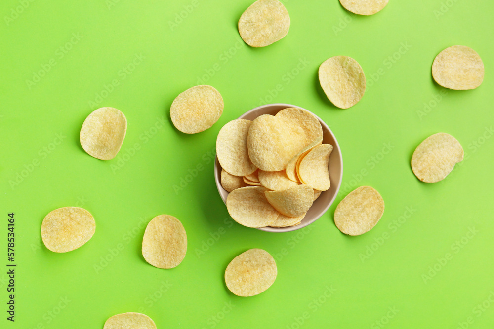 Bowl with delicious potato chips on green background