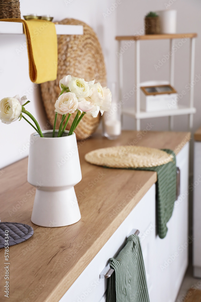 Vase with ranunculus flowers on counter in light kitchen