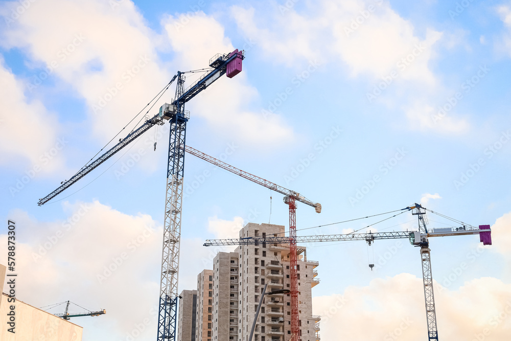 View of construction cranes and unfinished buildings on sunny day