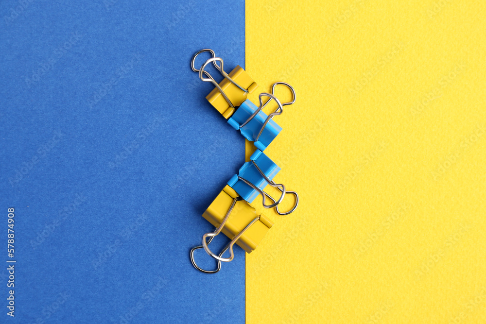 Blue and yellow binder clips on color background