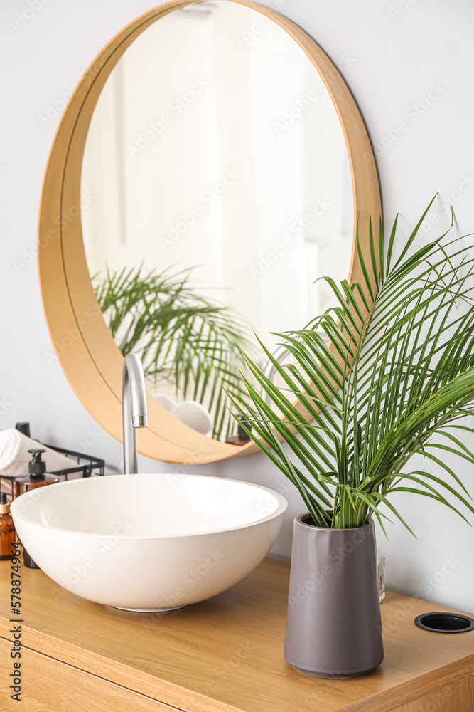 Vase with palm leaves and sink on table in bathroom