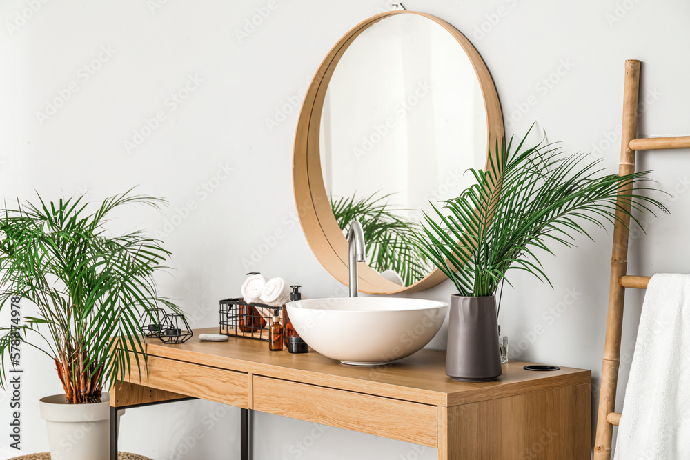 Vase with palm leaves, sink and cosmetic products on table in bathroom