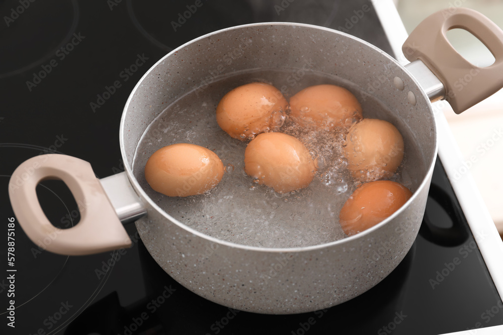 Cooking pot with boiling eggs on stove in kitchen