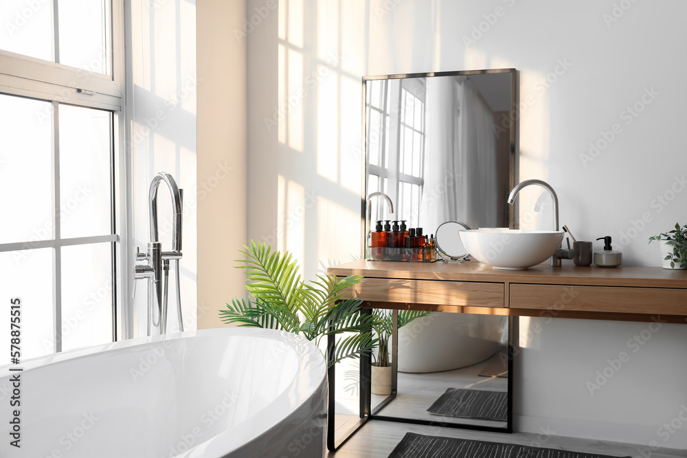 Interior of light bathroom with bathtub, table and mirror