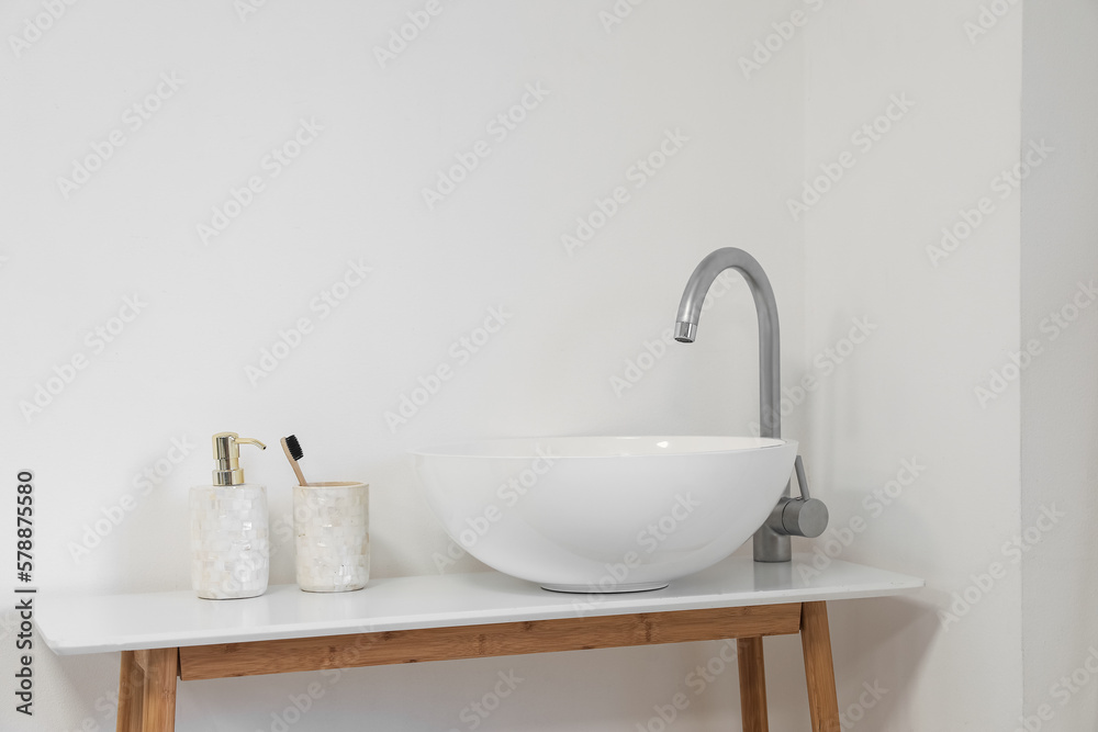 Sink with soap bottle and toothbrush on table in light bathroom