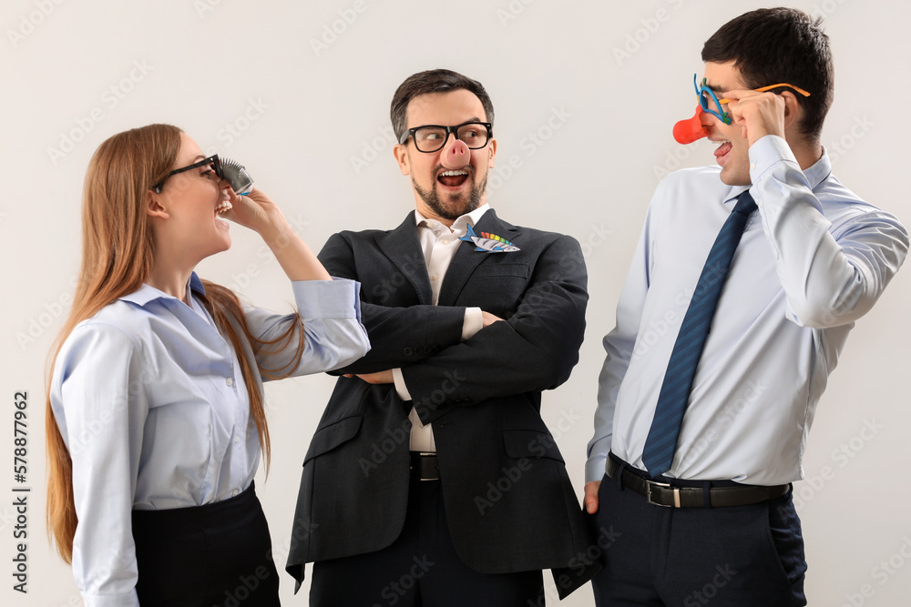 Business colleagues in funny disguise on light background. April Fools Day celebration