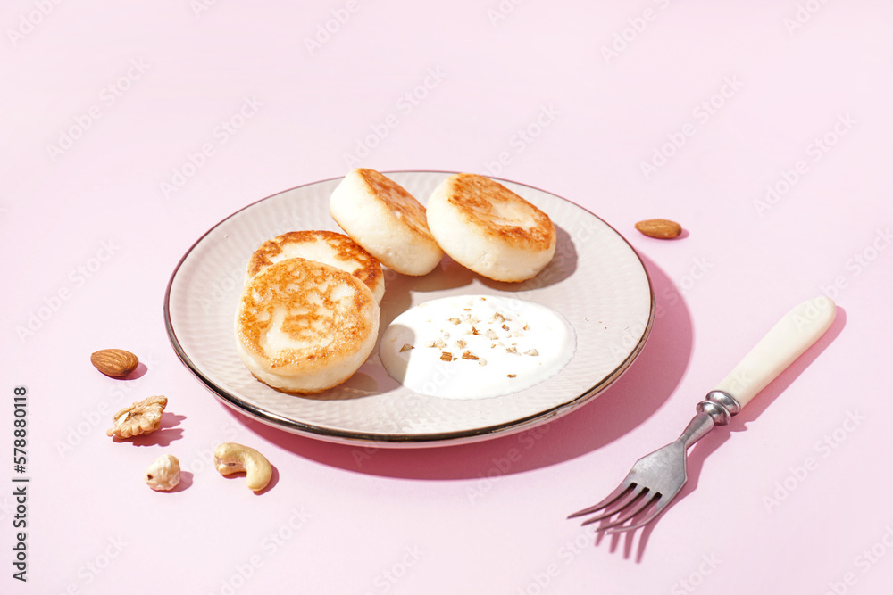 Plate with tasty cottage cheese pancakes and sour cream on pink background