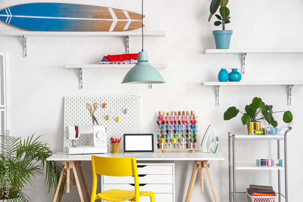 Interior of modern atelier with tailors workplace, shelves and surfboard