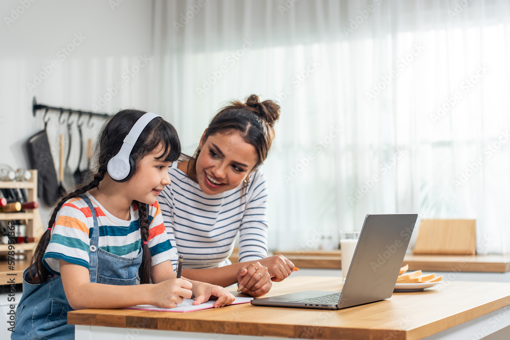 Caucasian young girl kid learning online class at home with mother. 