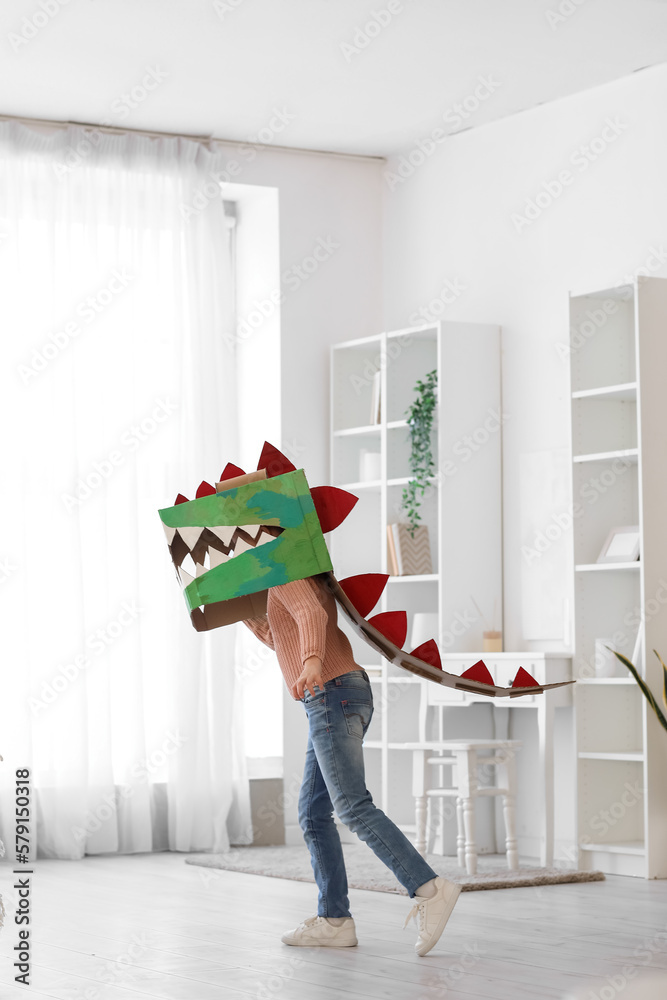 Little girl in cardboard dinosaur costume playing at home