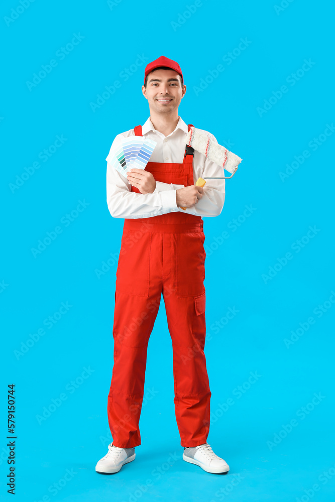 Male painter with color palettes and roller on blue background