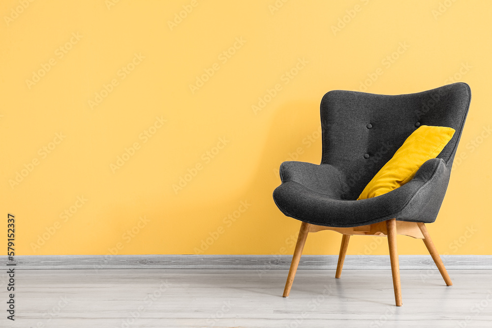 Stylish grey armchair with cushion near yellow wall