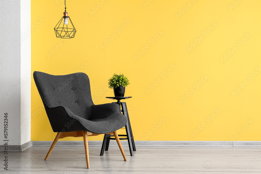 Stylish grey armchair and end table with houseplant near yellow wall