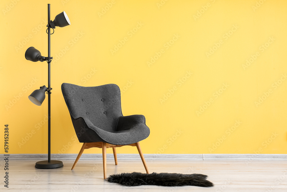 Stylish grey armchair, black fur rug and lamps near yellow wall