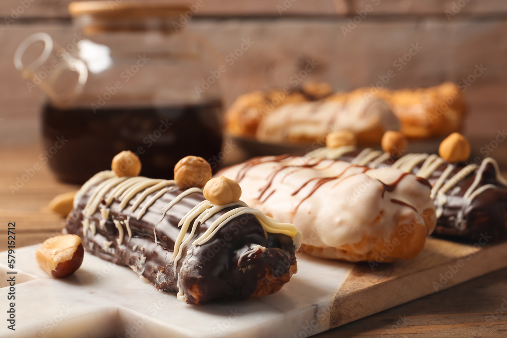 Board with delicious eclairs on wooden table, closeup